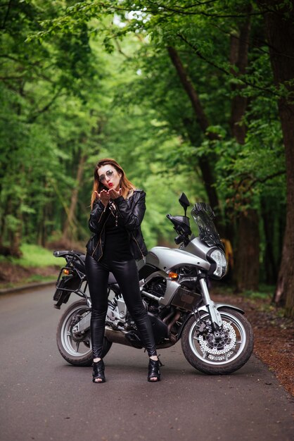 Una atractiva chica sexy vestida de cuero posando cerca de una motocicleta deportiva afuera