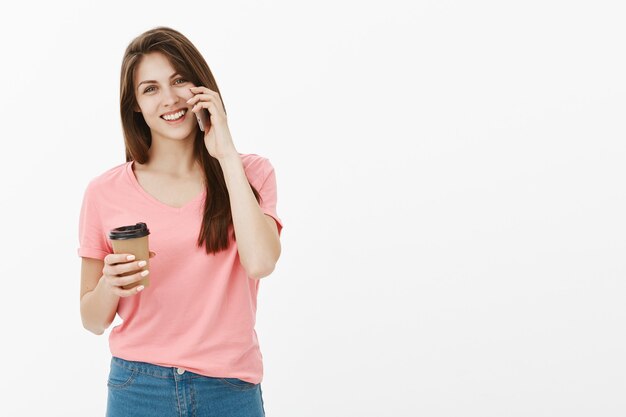 Atractiva chica sonriente hablando felizmente por teléfono y tomando café