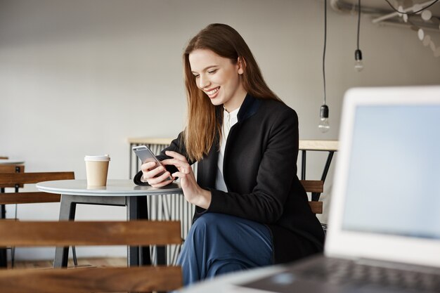 Atractiva empresaria elegante esperando en la cafetería, mediante teléfono móvil