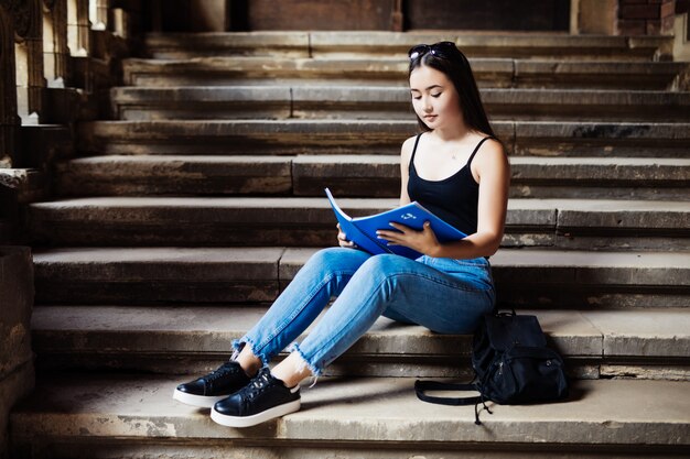 Atractiva estudiante universitaria sentada en las escaleras en el campus