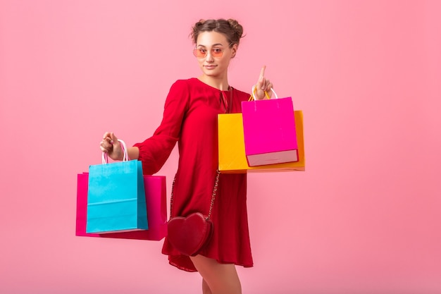 Atractiva feliz divertida emoción elegante mujer adicta a las compras en vestido rojo de moda con coloridas bolsas de la compra en la pared rosa aislada, venta emocionada, tendencia de moda primavera verano