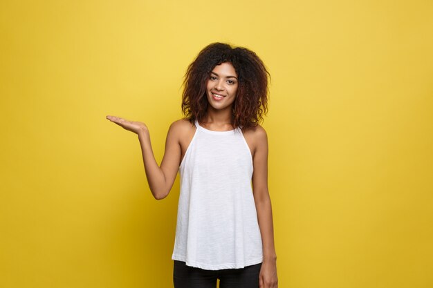 Atractiva hermosa mujer afroamericana posting jugar con su cabello rizado afro. Fondo amarillo del estudio. Espacio De La Copia.