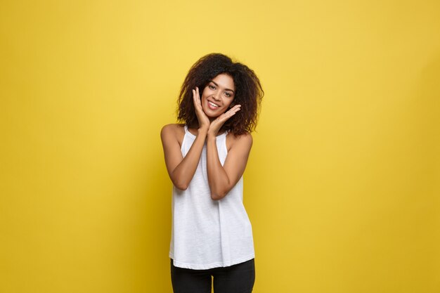Atractiva hermosa mujer afroamericana posting jugar con su cabello rizado afro. Fondo amarillo del estudio. Espacio De La Copia.
