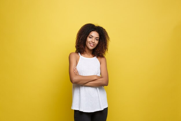 Atractiva hermosa mujer afroamericana posting jugar con su cabello rizado afro. Fondo amarillo del estudio. Espacio De La Copia.