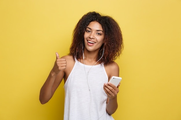 Atractiva hermosa mujer afroamericana posting jugar con su cabello rizado afro. Fondo amarillo del estudio. Espacio De La Copia.