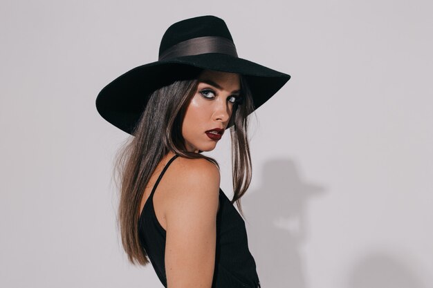 Atractiva hermosa mujer elegante con maquillaje de noche con sombrero mirando a la cámara