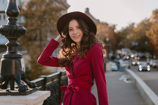 Atractiva hermosa mujer elegante en traje morado caminando en las calles de la ciudad, tendencia de moda primavera verano otoño temporada con sombrero, sosteniendo el bolso