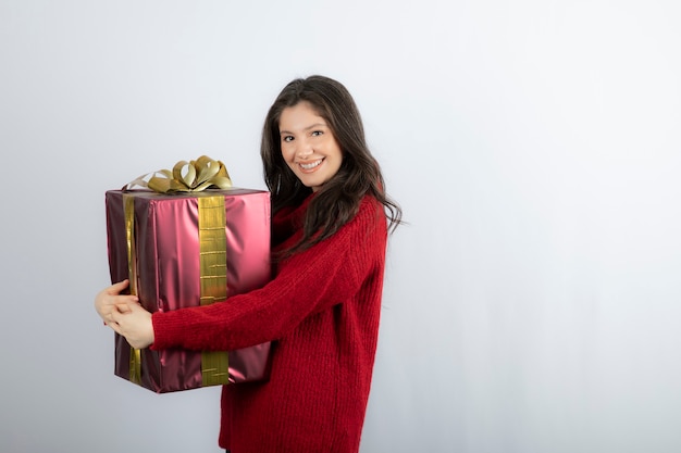 Una atractiva joven abrazando un regalo de Navidad sobre una pared blanca.