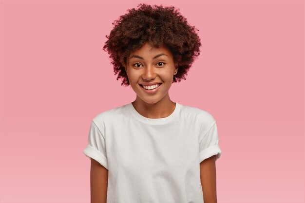 Atractiva joven afroamericana con una tierna sonrisa dentuda, muestra dientes blancos, vestida con una camiseta informal