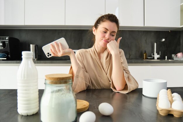 Atractiva joven alegre horneando en la cocina haciendo masa sosteniendo un libro de recetas con ideas