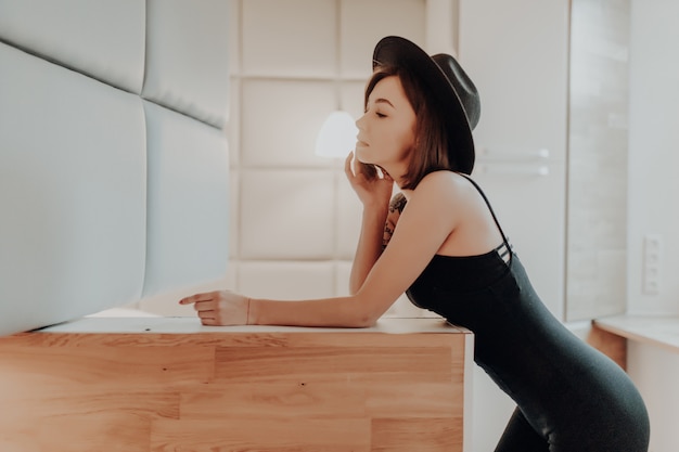 Atractiva joven morena adulta está posando en vestido negro en el apartamento de moda