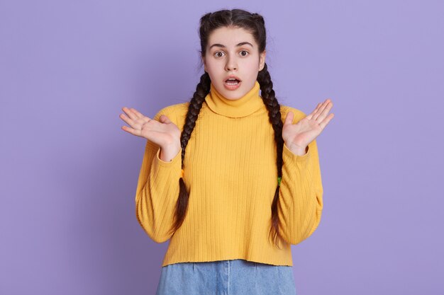 Atractiva joven morena con dos coletas posando en suéter amarillo contra la pared de color lila