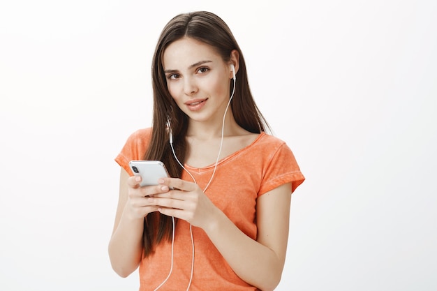 Atractiva joven morena escuchando música en auriculares y sosteniendo el teléfono móvil