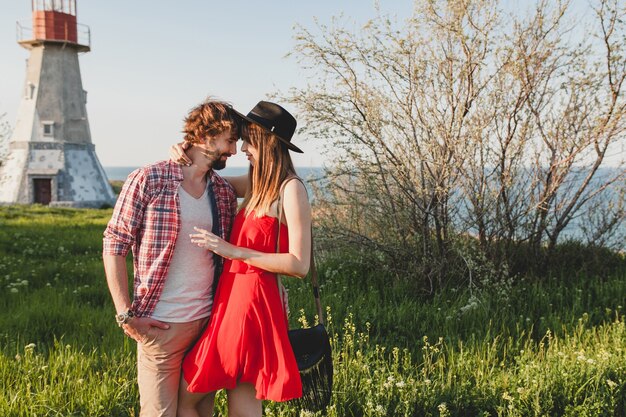 Atractiva joven pareja elegante enamorada en el campo, estilo bohemio indie hipster, vacaciones de fin de semana, traje de verano, vestido rojo, hierba verde