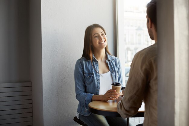 Atractiva joven en ropa elegante en una cita en la cafetería, escuchando a su pareja con expresión feliz y emocionada. Estilo de vida, concepto de relación.