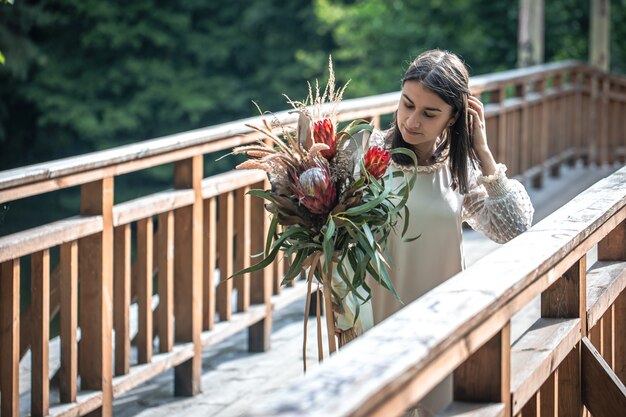 Una atractiva joven sobre un puente de madera se encuentra con un ramo de flores exóticas.