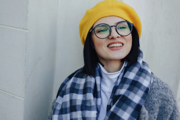 Atractiva joven sonriente con gafas en abrigo y boina amarilla