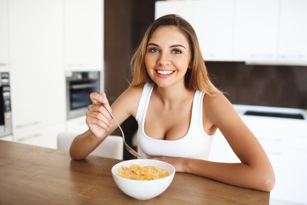 Atractiva jovencita comiendo copos de maíz con leche sonriendo