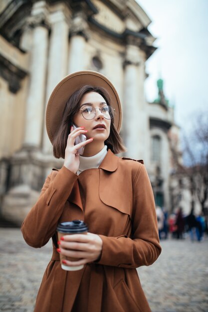 Atractiva jovencita hablando por teléfono móvil caminando al aire libre en un frío día de otoño