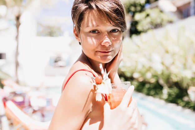 Atractiva modelo femenina de pelo corto disfrutando de un cóctel de frutas.