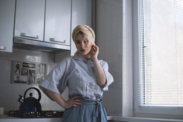 Atractiva modelo femenina rubia con un pañuelo en la cabeza posando en la cocina