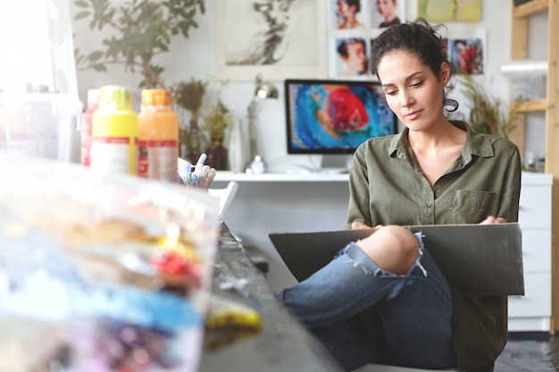 Atractiva morena joven artista europea que expresa sus ideas a través de la pintura, se siente feliz por su ocupación, disfruta el proceso de crear algo nuevo. Arte, artesanía y creatividad.