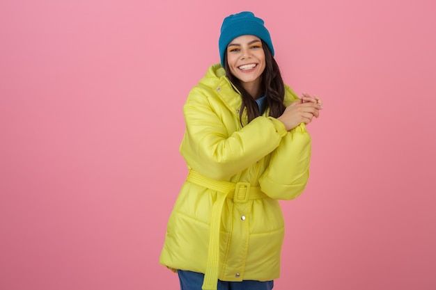 Atractiva mujer activa posando en una pared rosada en una colorida chaqueta de invierno de color amarillo brillante, divertida sonrisa, tendencia de moda de abrigo cálido, expresión de la cara de sorpresa sorprendida loca