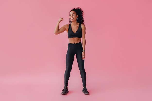 Atractiva mujer afroamericana negra en traje de fitness leggins negros sobre fondo rosa