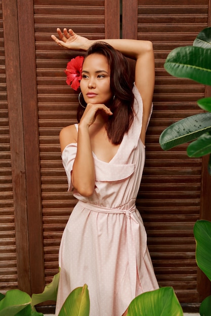 Atractiva mujer asiática con flor de hibisco en pelos posando en jardín tropical.