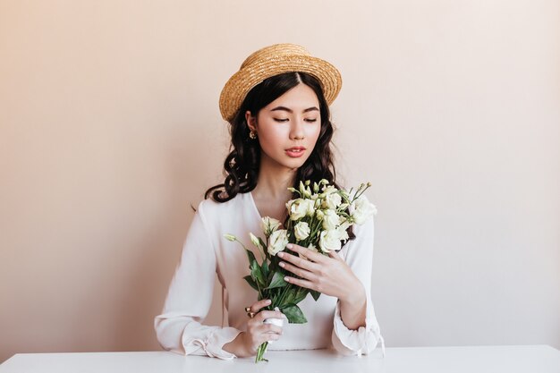 Atractiva mujer asiática con flores blancas. Disparo de estudio de modelo chino dichoso con ramo de eustoma.