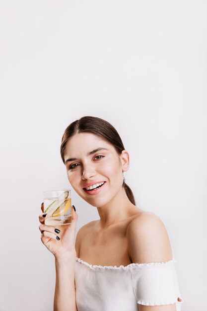 La atractiva mujer de cabello oscuro está llena de energía y sonrisas. Señora sosteniendo un vaso de agua con limón.