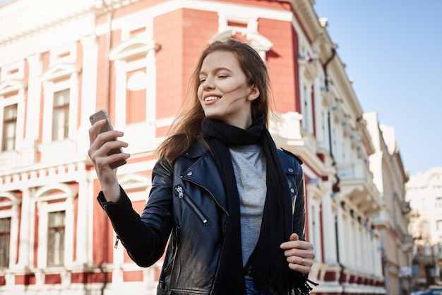 atractiva mujer caminando por la ciudad, sosteniendo el teléfono inteligente