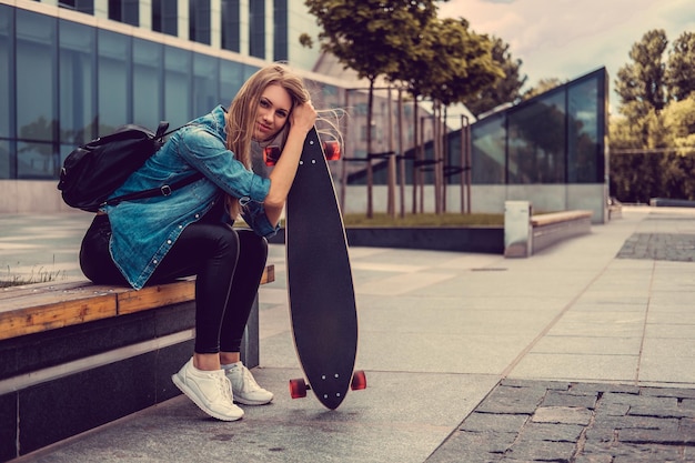 Atractiva mujer casual rubia se sienta en los escalones y sostiene Longboard.