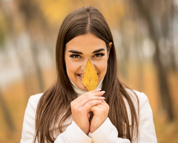 Atractiva mujer caucásica sonriendo y sosteniendo una hoja caída en el otoño