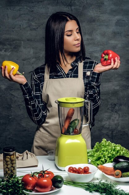 Atractiva mujer chef morena sostiene pimientos dulces y coloridos para un cóctel de verduras.