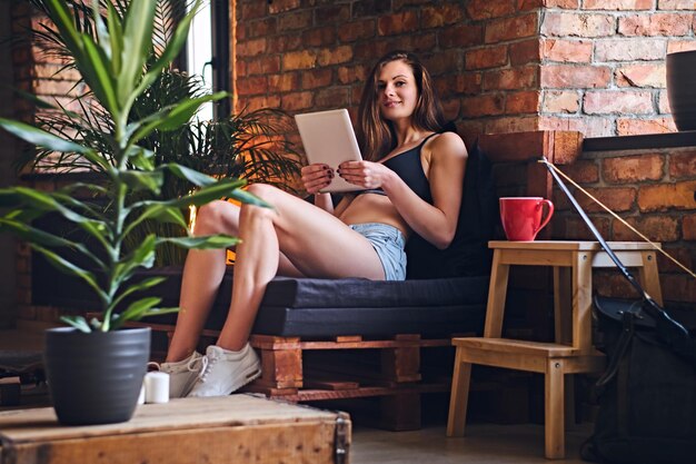 Atractiva mujer deportiva que usa tabletas y bebe café en la habitación interior del loft.