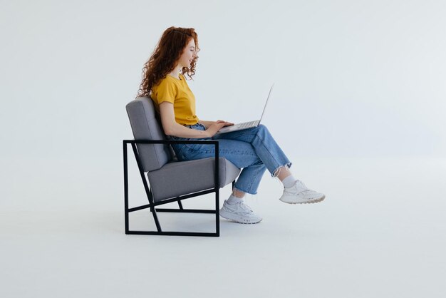 Atractiva mujer edhead sentada en el suelo con las piernas cruzadas sosteniendo vueltas portátiles trabajando en aire fresco escribiendo un nuevo programa freelance sobre fondo blanco