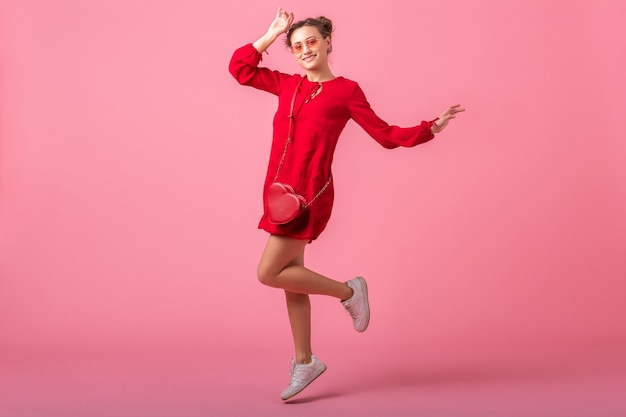 Atractiva mujer elegante sonriente feliz en vestido rojo de moda saltando corriendo en la pared rosa aislada, tendencia de moda primavera verano, chica coqueta de humor romántico