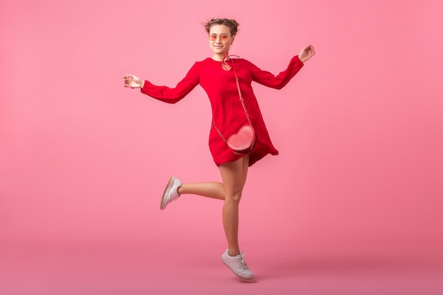 Atractiva mujer elegante sonriente feliz en vestido rojo de moda saltando corriendo en la pared rosa aislada, tendencia de moda primavera verano, día de Santa valenita, chica coqueta de humor romántico