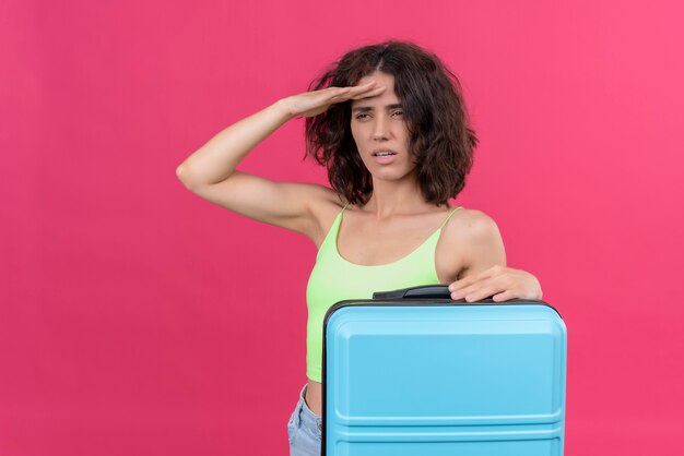 Una atractiva mujer encantadora con pelo corto vistiendo verde crop top sosteniendo maleta azul