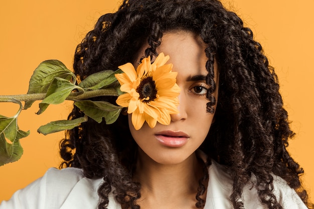 Foto gratuita atractiva mujer étnica con flor cubriendo ojo.