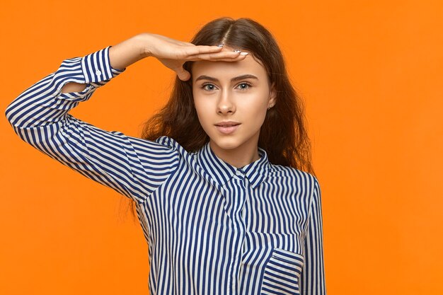 Atractiva mujer europea joven linda con el pelo largo suelto posando en la pared amarilla del estudio manteniendo la mano