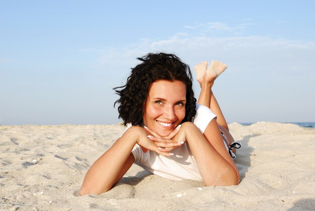 Atractiva mujer feliz acostada en la playa y mirando a la cámara