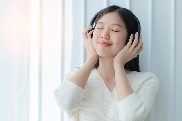 Atractiva mujer hermosa asiática disfruta de la música de los auriculares con felicidad y alegría. Retrato de una mujer asiática vestida de blanco.