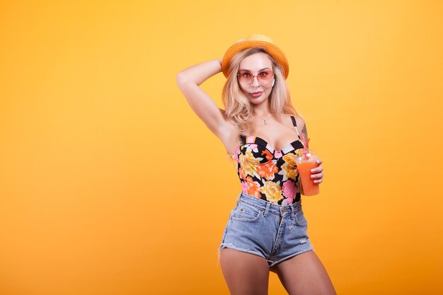 Atractiva mujer joven bebiendo jugo de naranja con gafas de sol en estudio