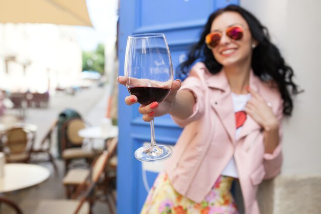 Atractiva mujer joven bebiendo vino en las vacaciones de verano sentado en el café de la calle de la ciudad en traje fresco