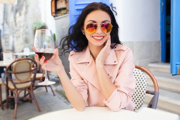 Foto gratuita atractiva mujer joven bebiendo vino en las vacaciones de verano sentado en el café de la calle de la ciudad en traje fresco