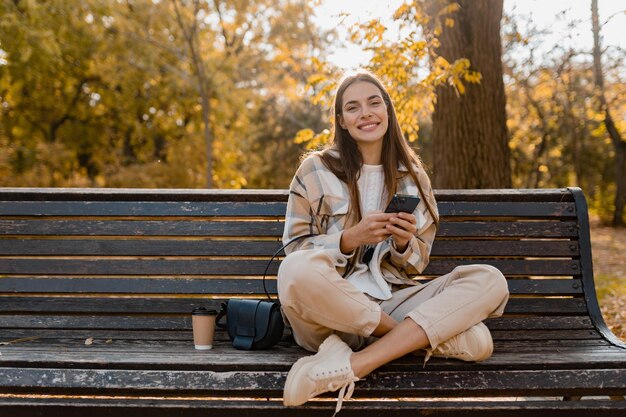 Atractiva mujer joven caminando en otoño con chaqueta usando el teléfono