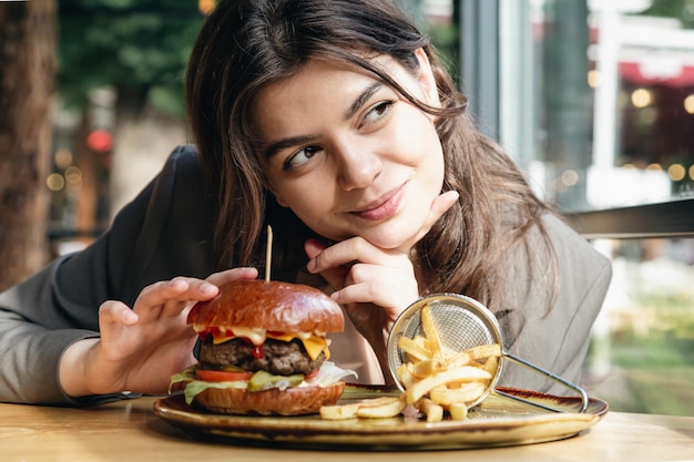 Atractiva mujer joven comiendo papas fritas y una hamburguesa en un restaurante