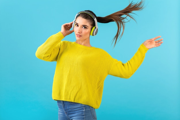 Atractiva mujer joven con estilo escuchando música en auriculares inalámbricos feliz vistiendo suéter de punto amarillo estilo colorido moda posando